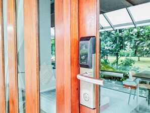 A modern door with a digital keypad and a keyhole, leading to a glass door that reveals a patio area with outdoor furniture and greenery.