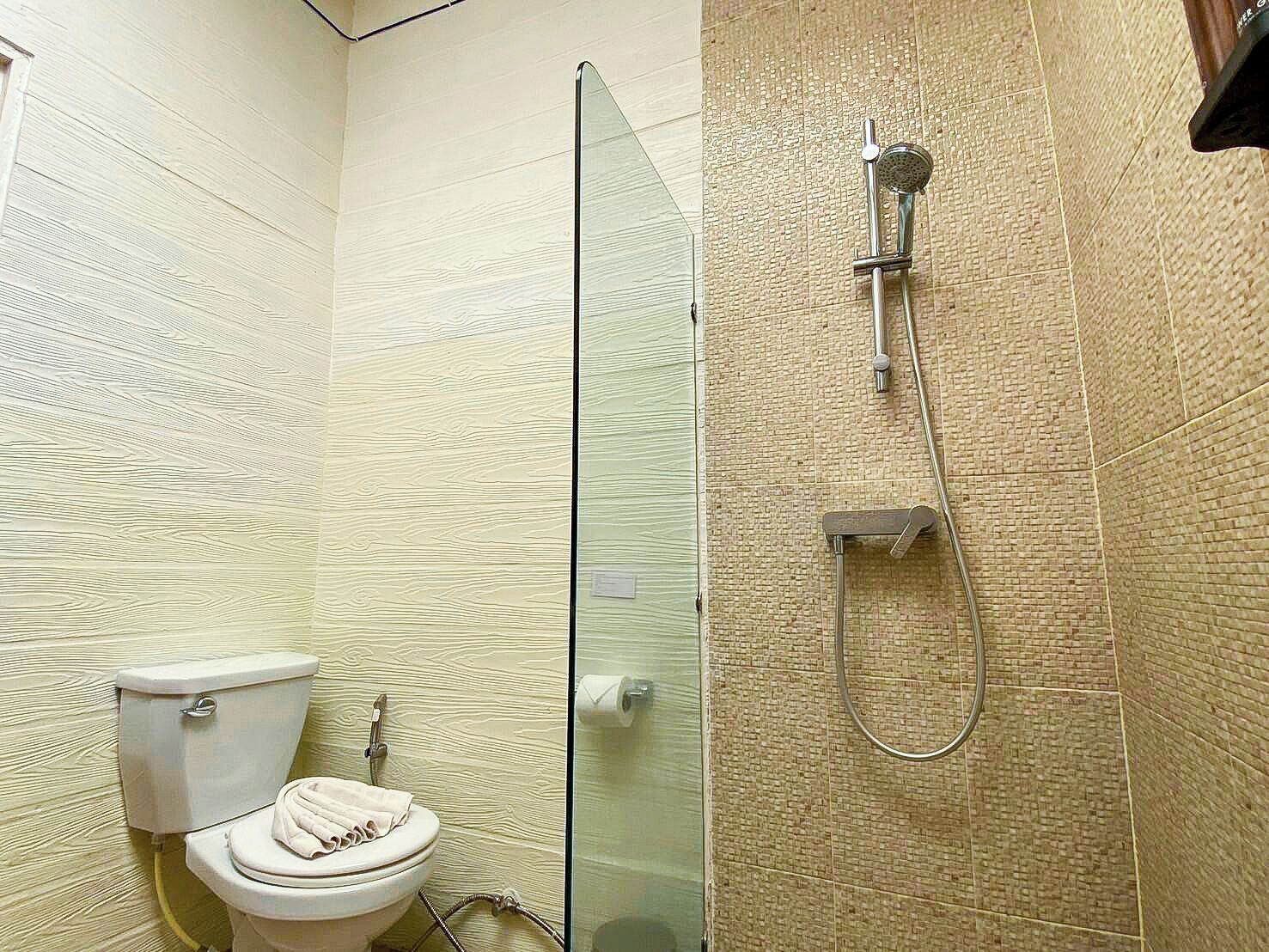 Et badeværelse med toilet, glasbrusekabine og brusehoved.