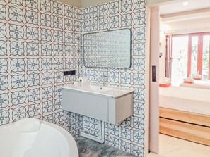 A bathroom with a patterned tile wall, a white sink, and a mirror.