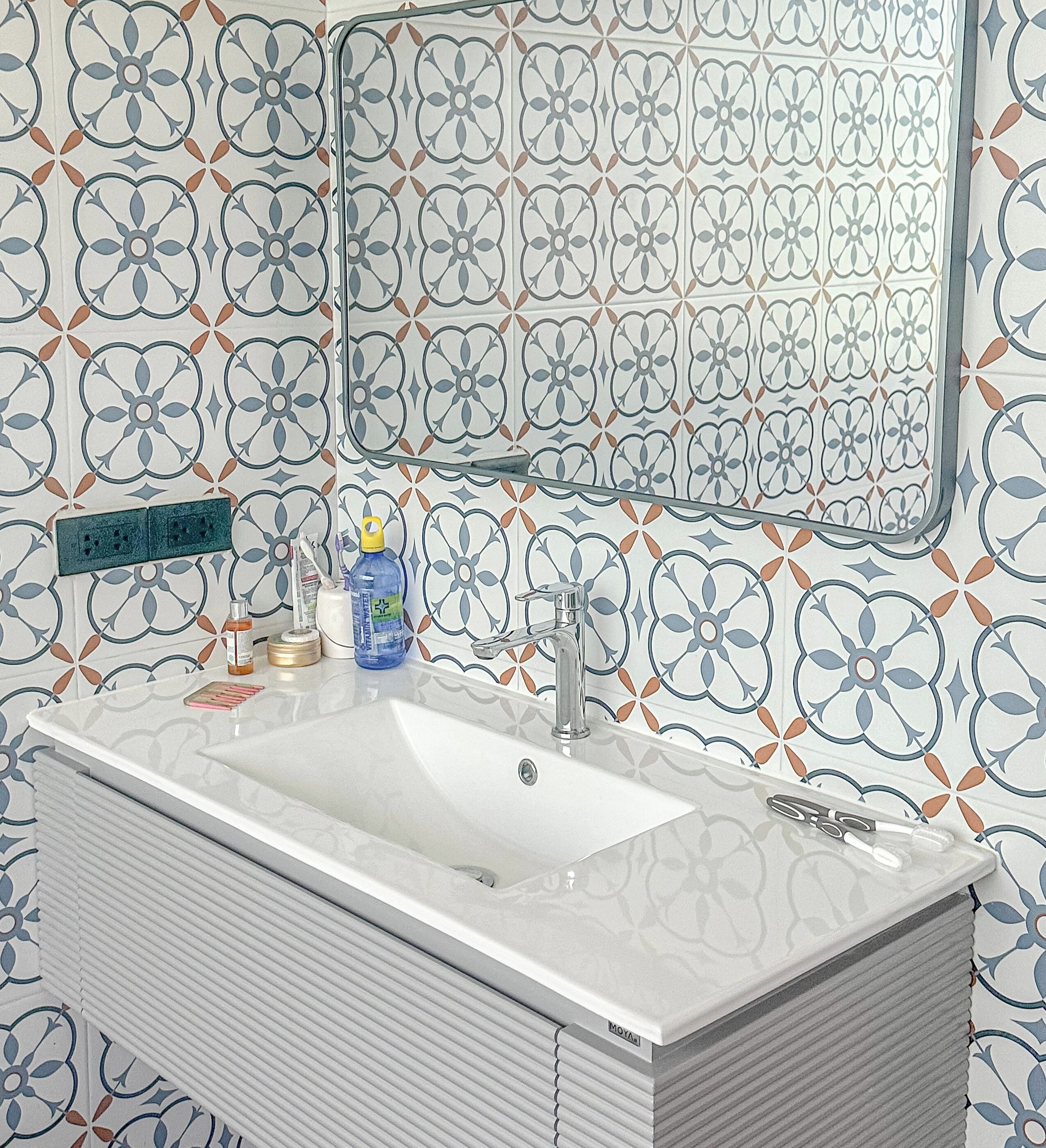 A bathroom with a white sink, a mirror, and patterned tiles on the walls.