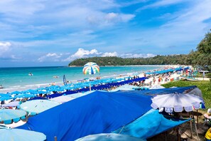A beach with numerous blue umbrellas and a large striped beach umbrella.