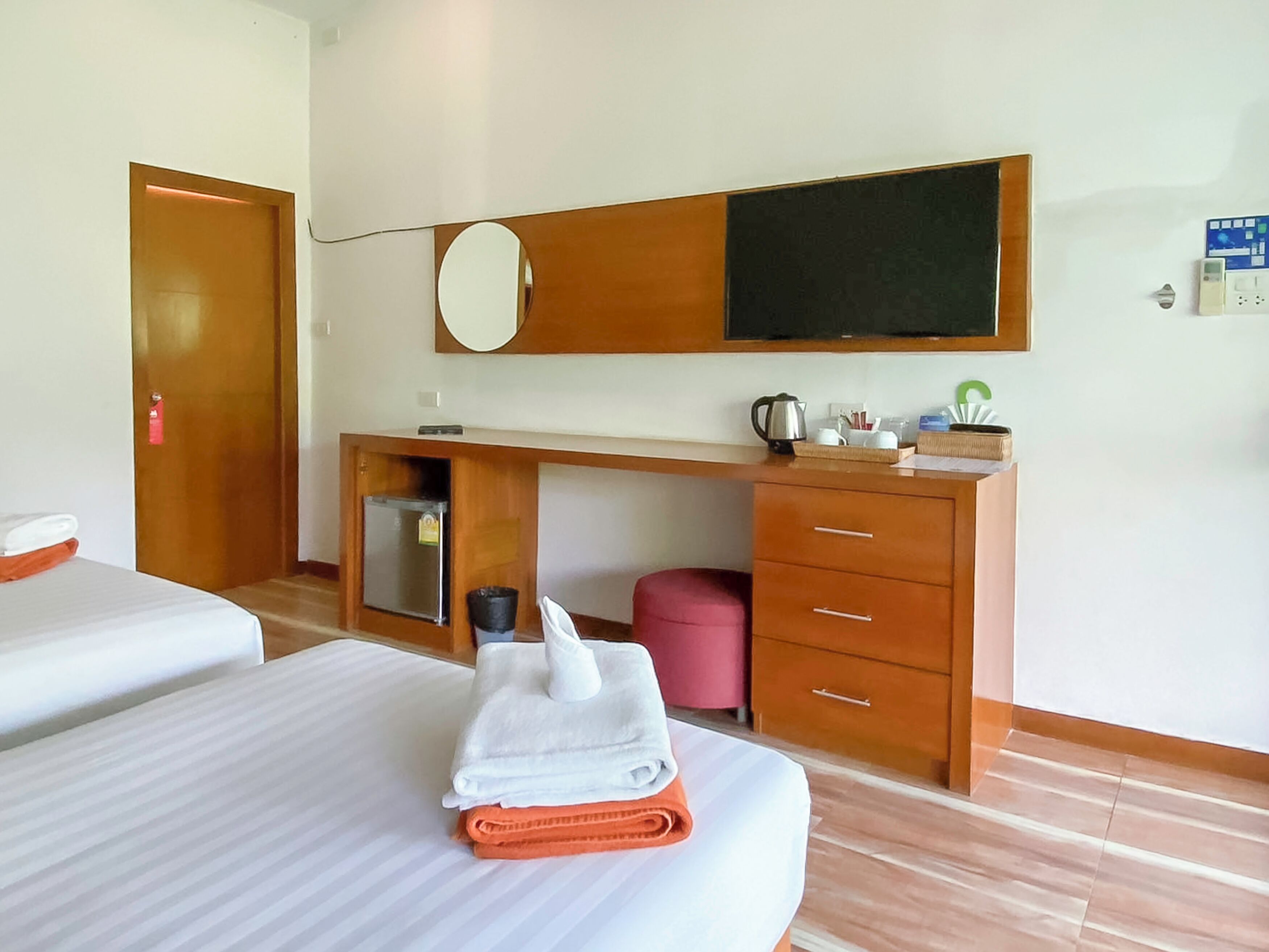 Ein Hotelzimmer mit zwei Betten, einem Holztisch, einer kleinen Kühlbox, einem Mülleimer und einem Spiegel.