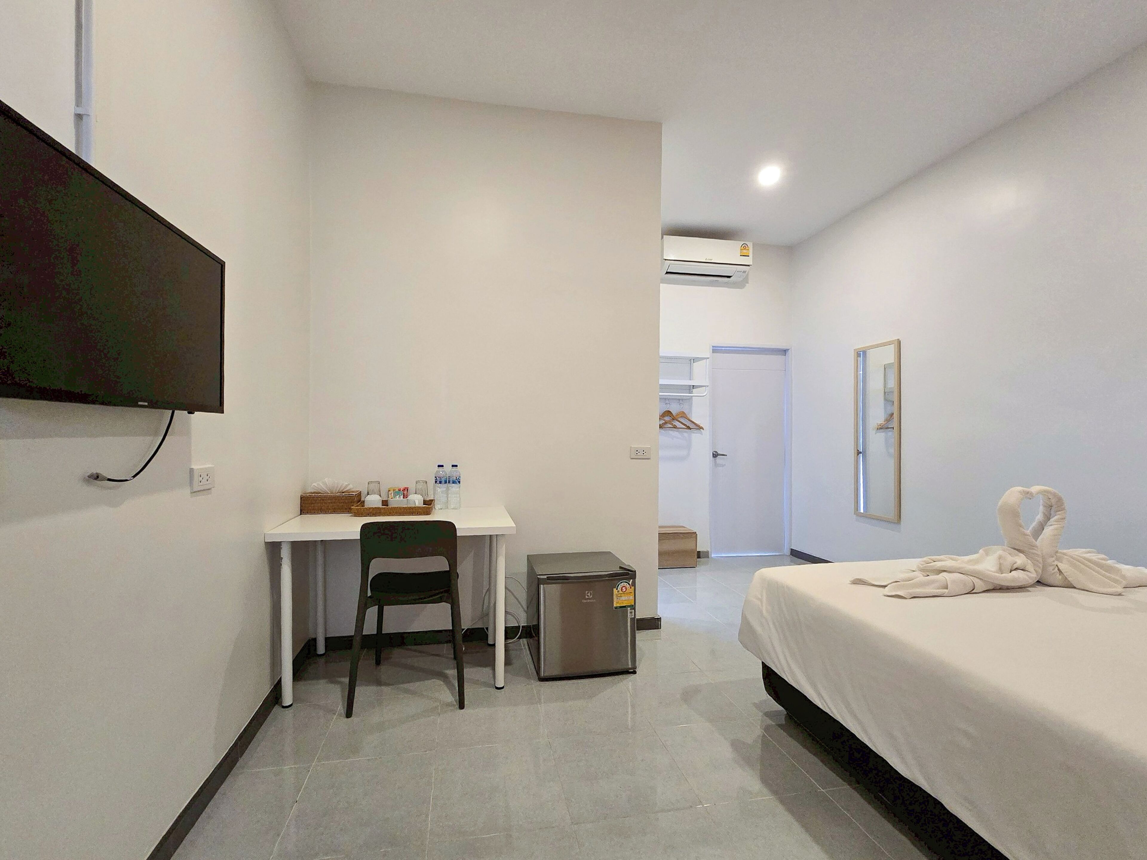A hotel room with a bed, a desk, a chair, a trash bin, a television, and a mirror.