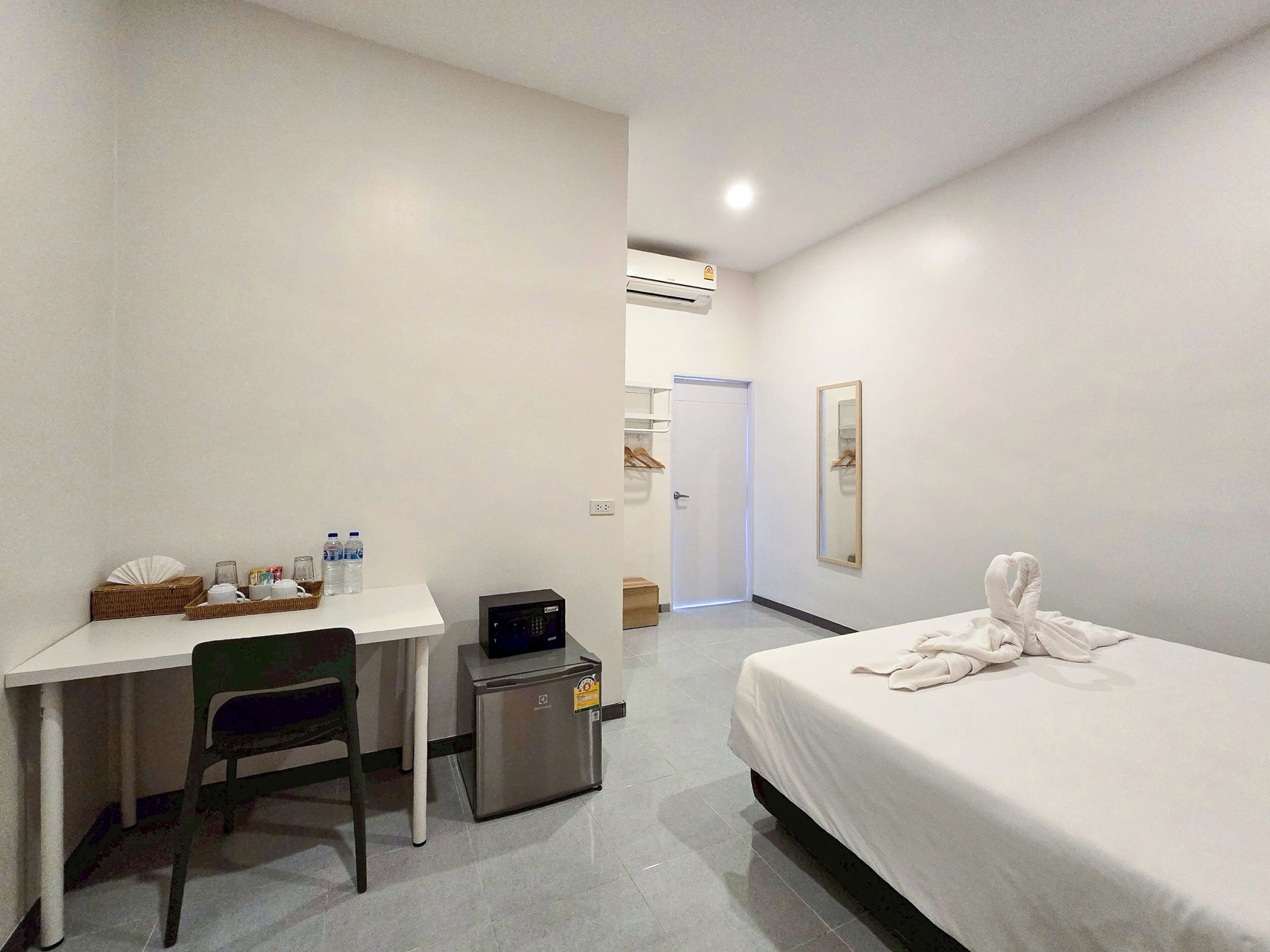 A hotel room with a bed, a desk with a chair, a small fridge, a microwave, a basket with toiletries, and a mirror on the wall.