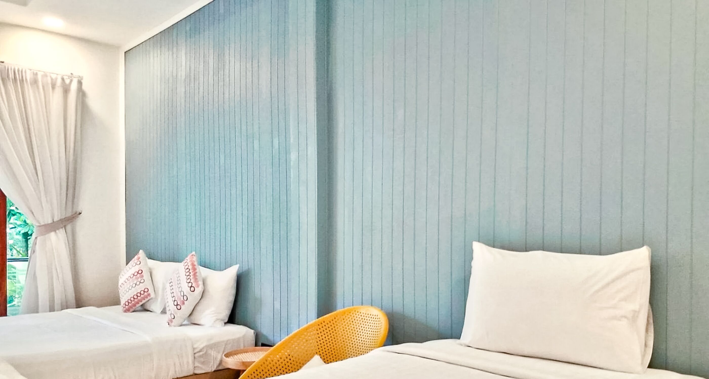 A bedroom with two beds, a blue wall, and a wicker chair.