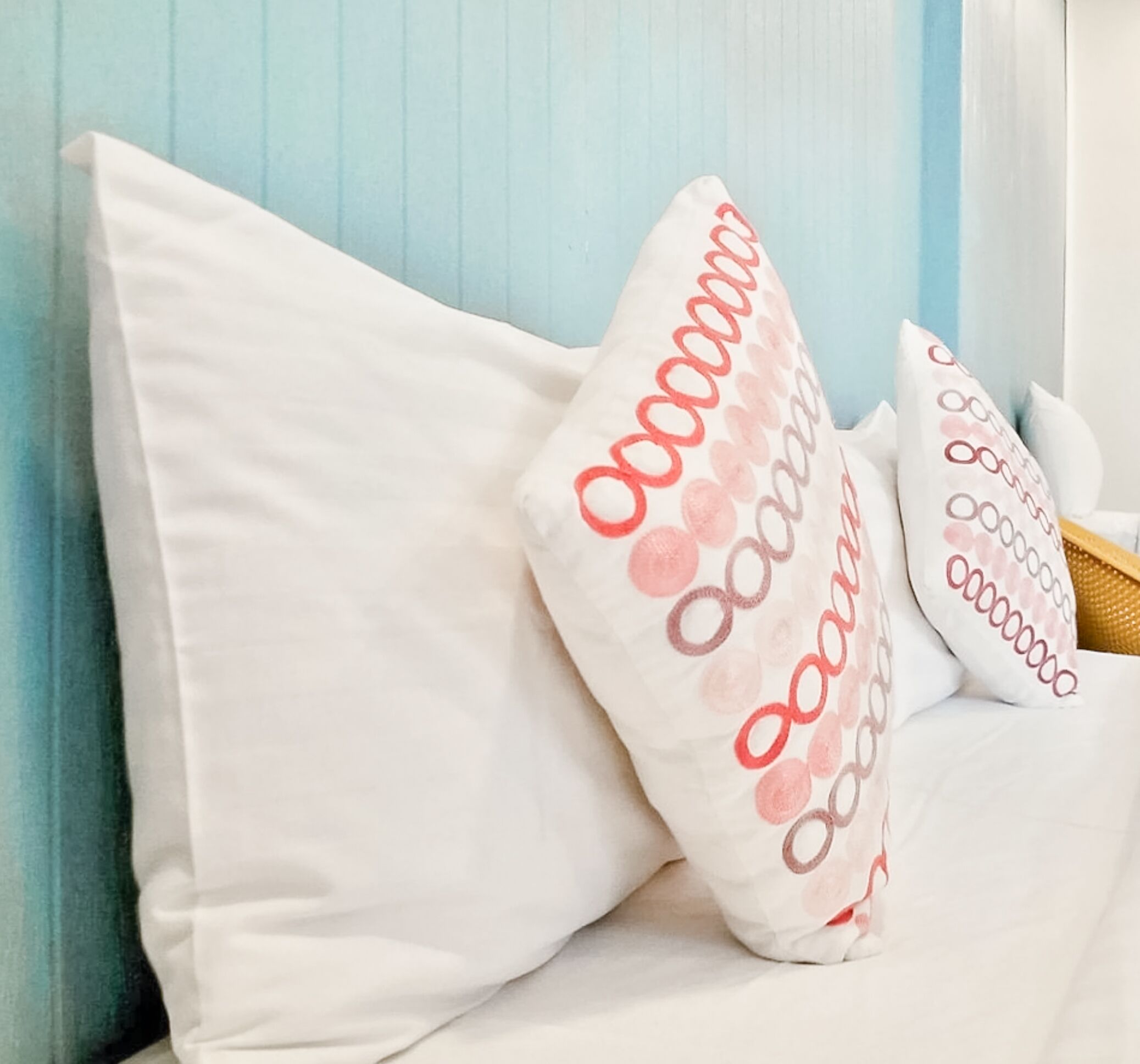 Una cama con almohadas blancas, una con texto rojo y otra con un estampado.