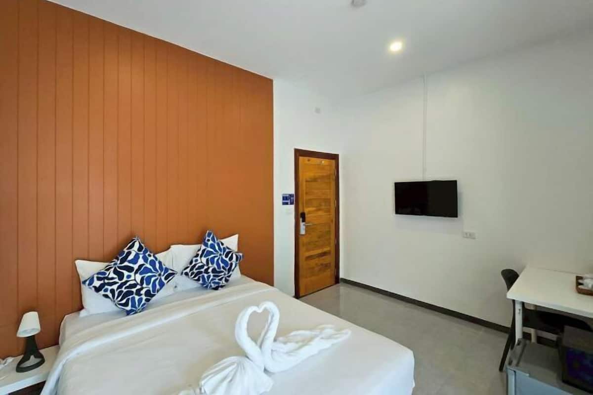 Une chambre d’hôtel avec un lit, un téléviseur fixé au mur, une porte en bois et une petite table.