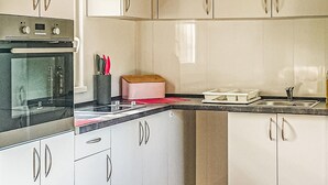 Eine Küche mit weißen Schränken, einem schwarzen Backofen, einer Spüle und einer Arbeitsplatte mit Schneidebrett und Besteck.