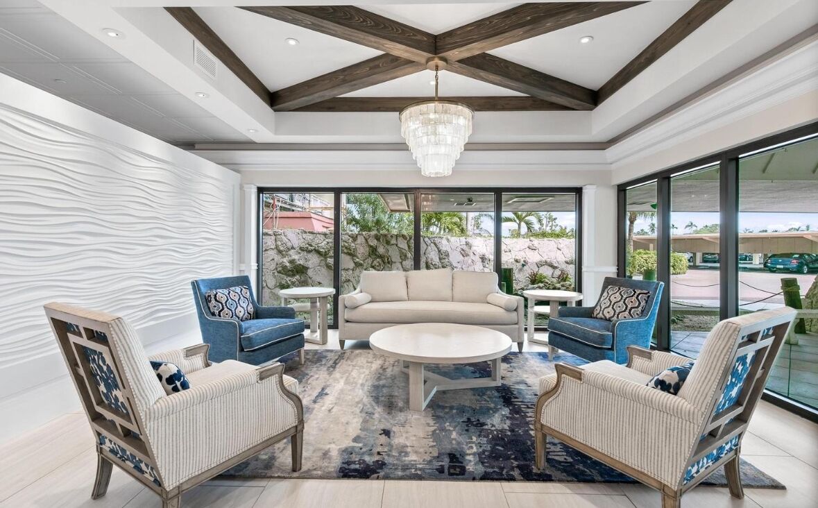 A spacious living area with a modern chandelier, a beige sofa, and blue patterned chairs.