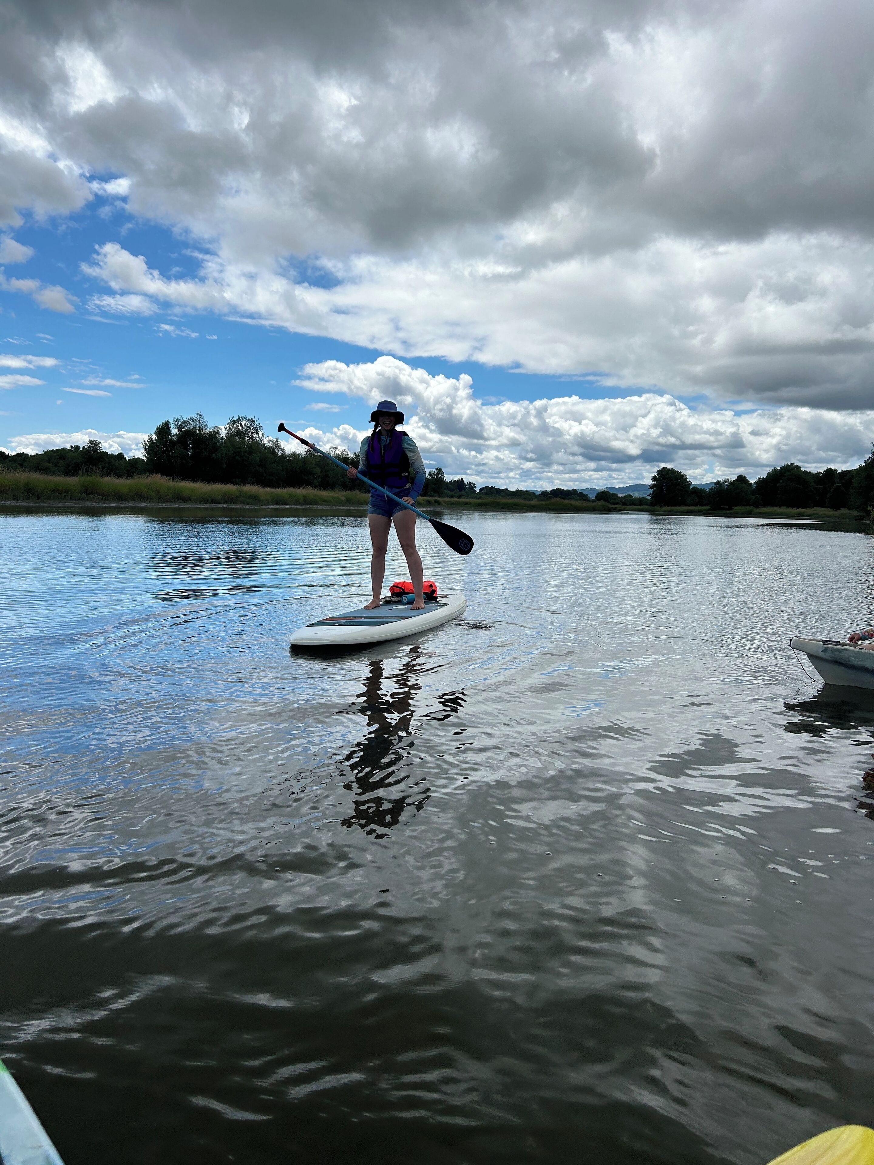A person standing on a paddleboard in a calm body of water, holding a paddle.