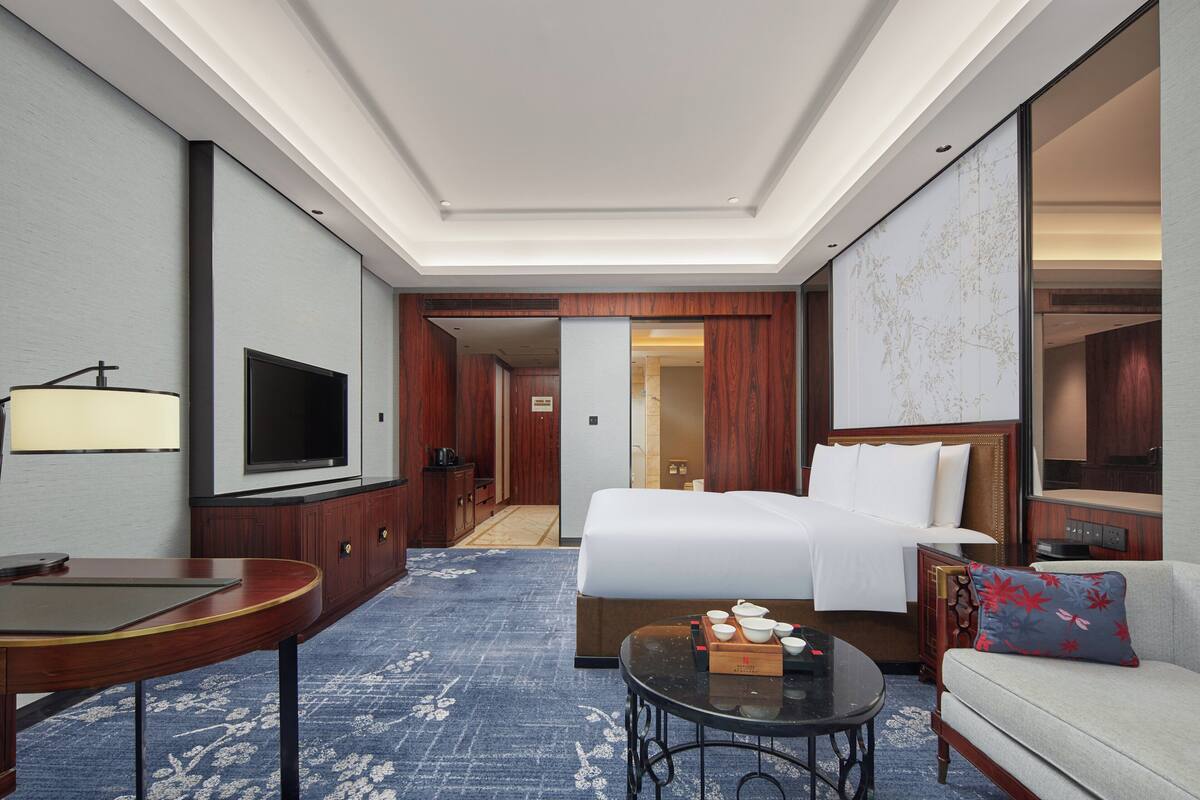 A hotel room with a bed, a sofa, a TV, a table, and a desk.
