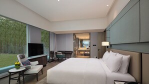 A modern hotel room with a large bed, a desk, a TV, and a view of greenery outside. - HUALUXE Leshan by IHG (Leshan)