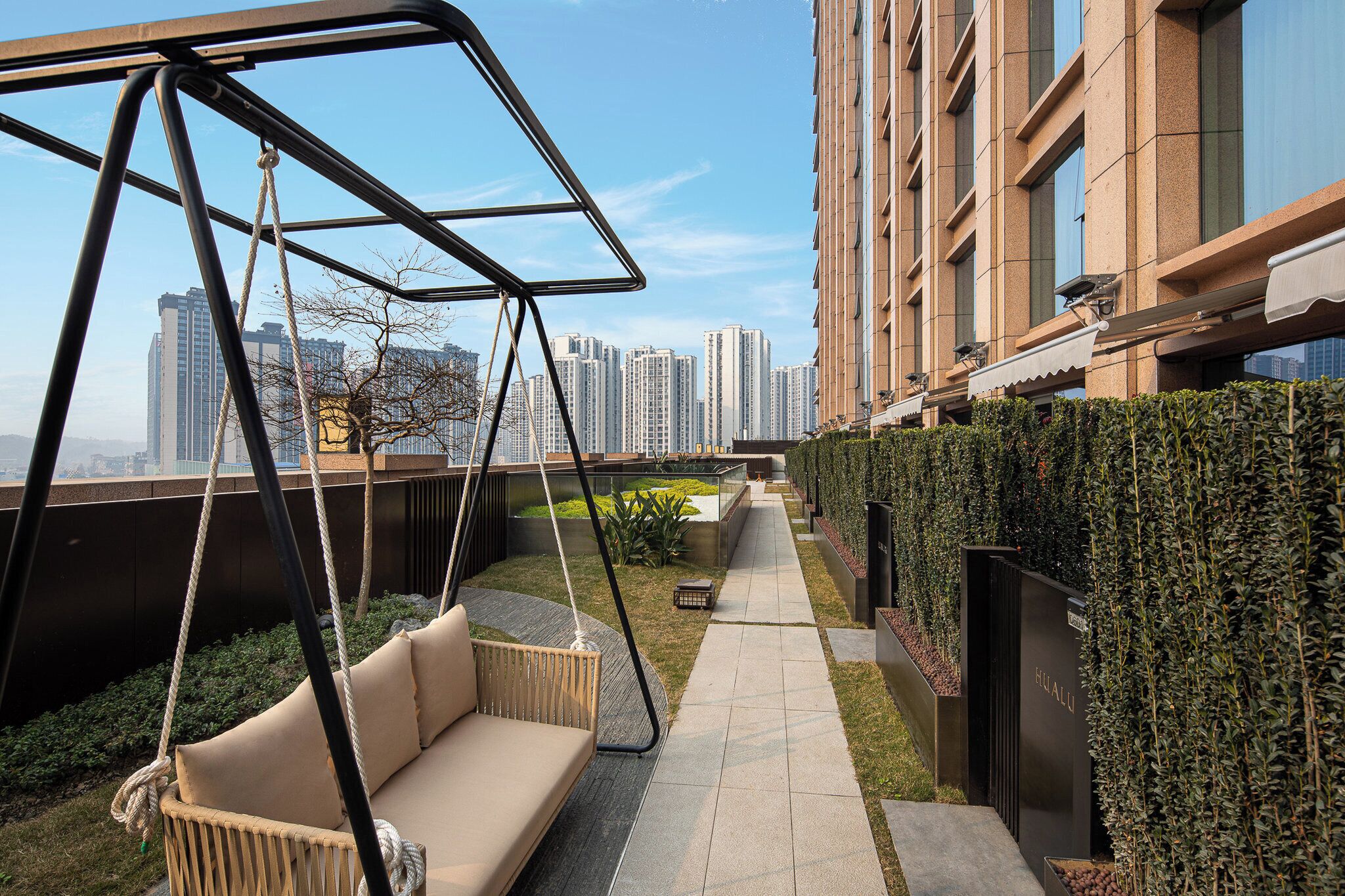 A rooftop terrace with a swing chair, a pathway, and a hedge.