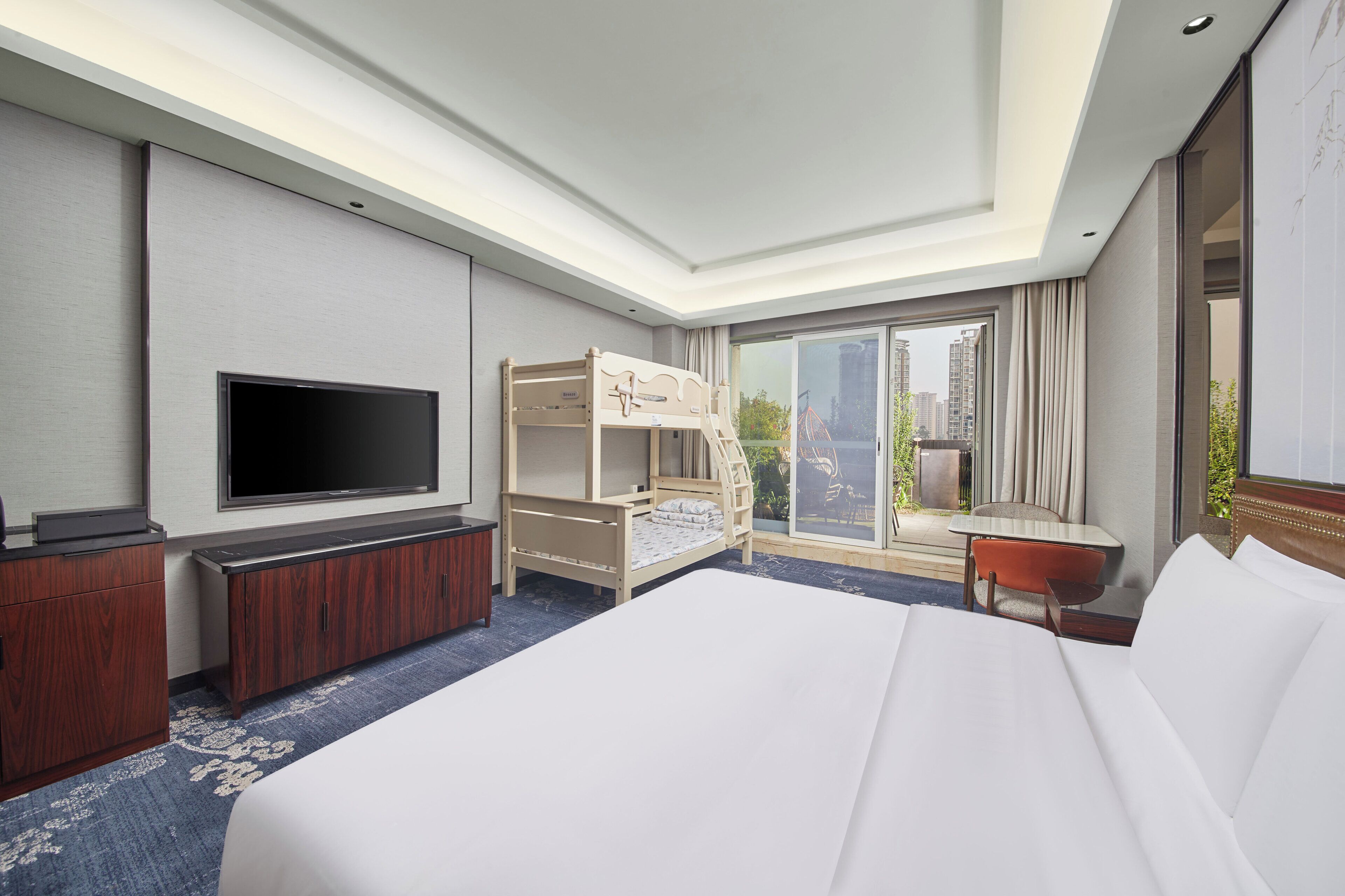 Habitación de hotel con una cama grande, televisor, litera, escritorio y vista de la ciudad.