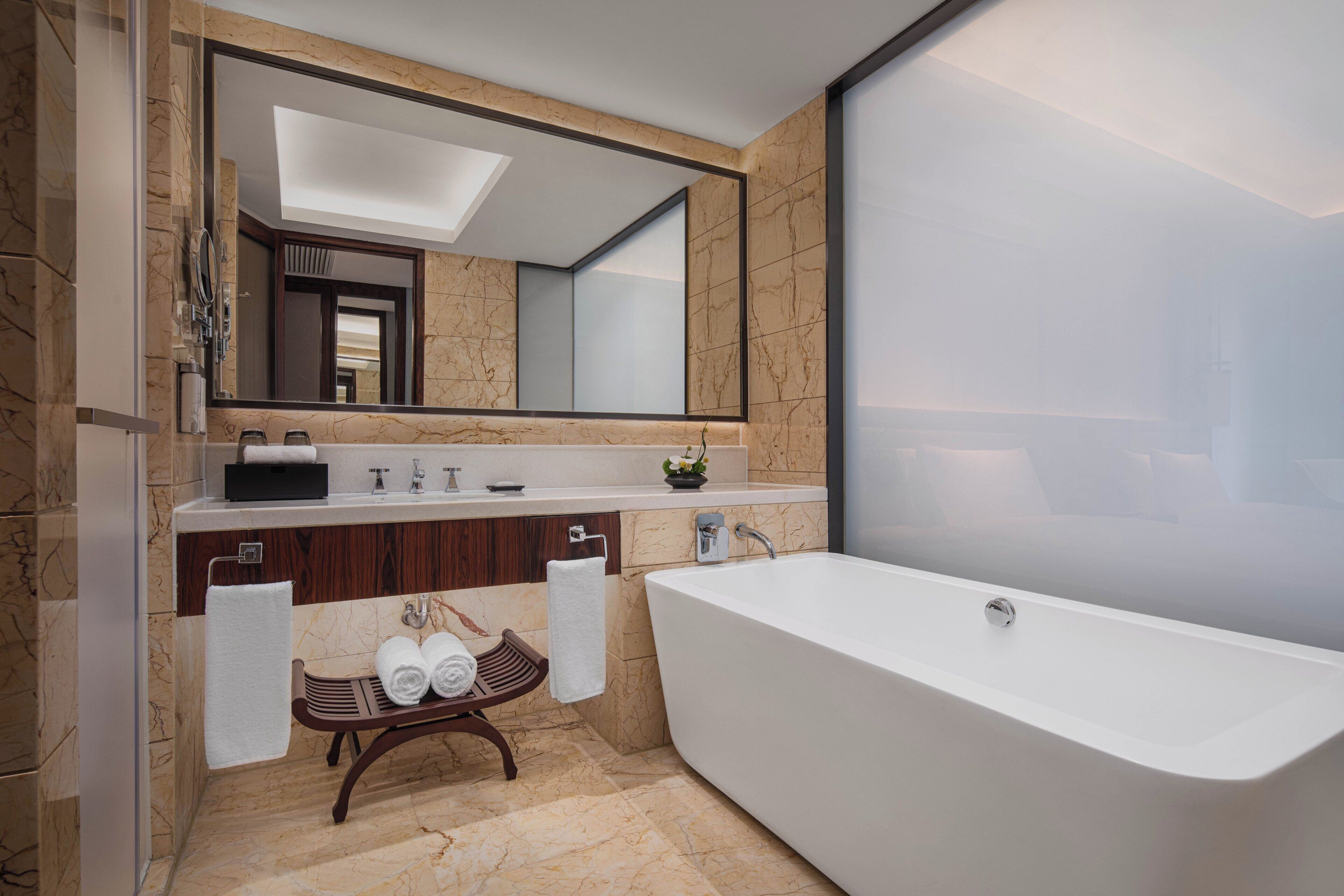 Un bany modern amb una banyera autònoma, un mirall gran i un lavabo amb taulell de marbre.