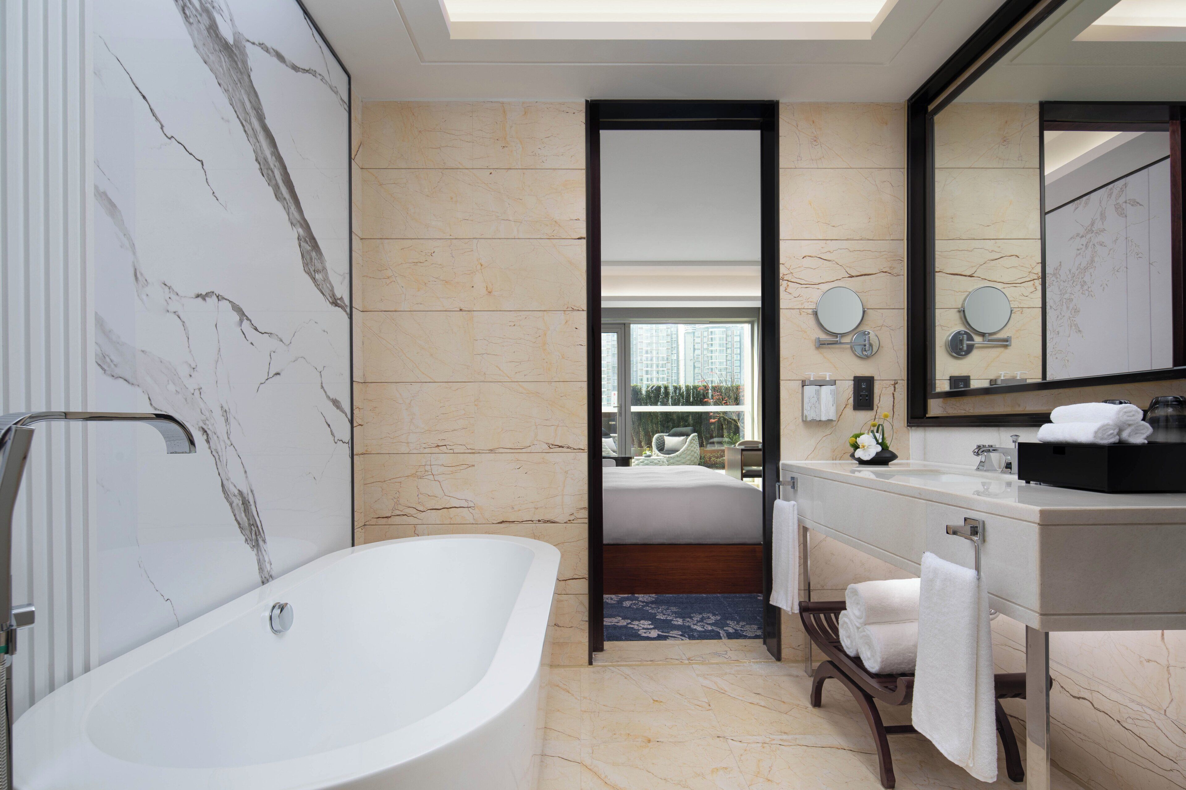 A modern bathroom with a freestanding bathtub, a large mirror, and a vanity with a sink and towel rack.