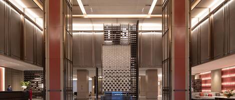 A spacious lobby with a central staircase, a reception desk, and a seating area with a sofa and coffee table.