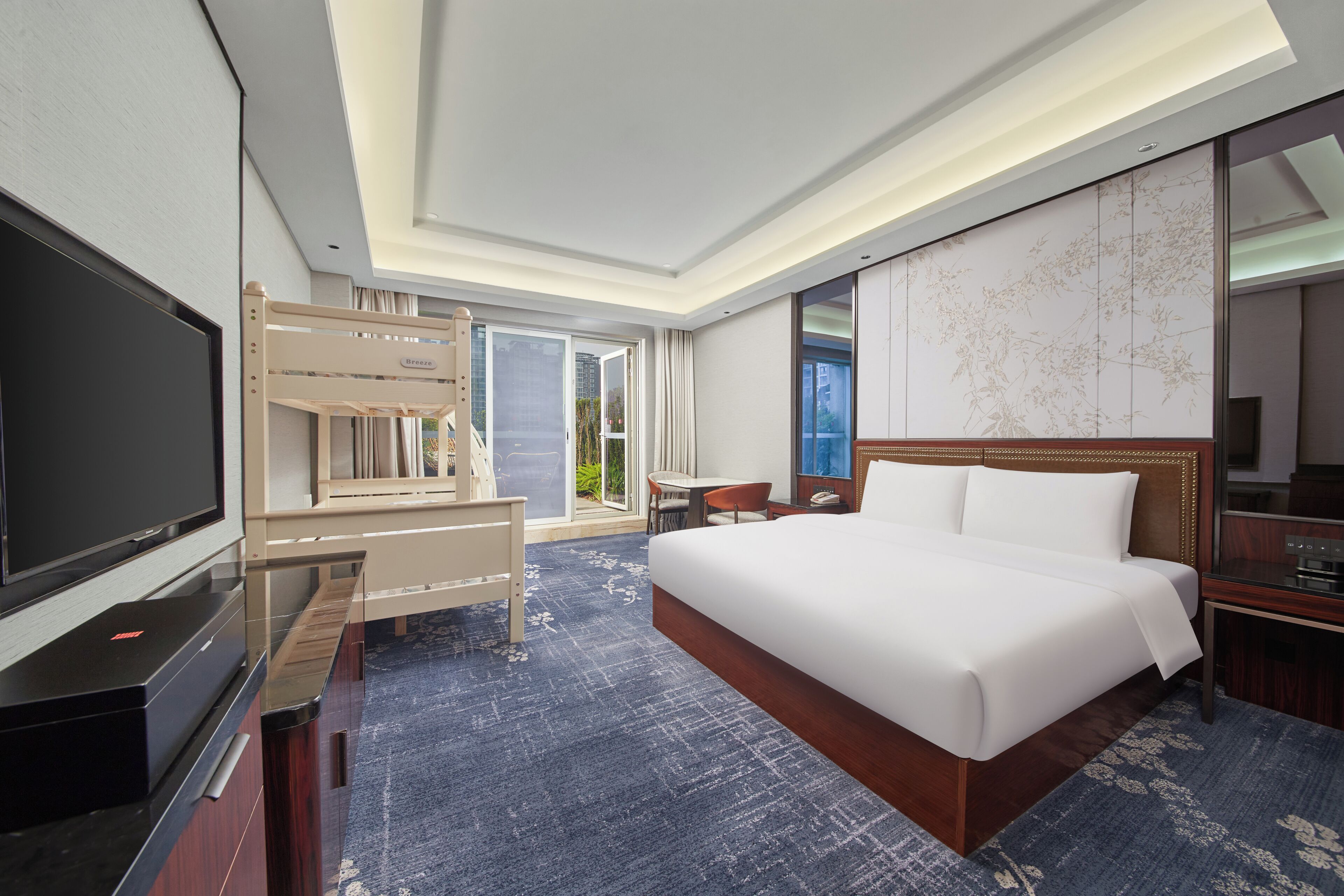 Una habitación de hotel con una cama grande, televisión, escritorio y balcón con vista a la ciudad.