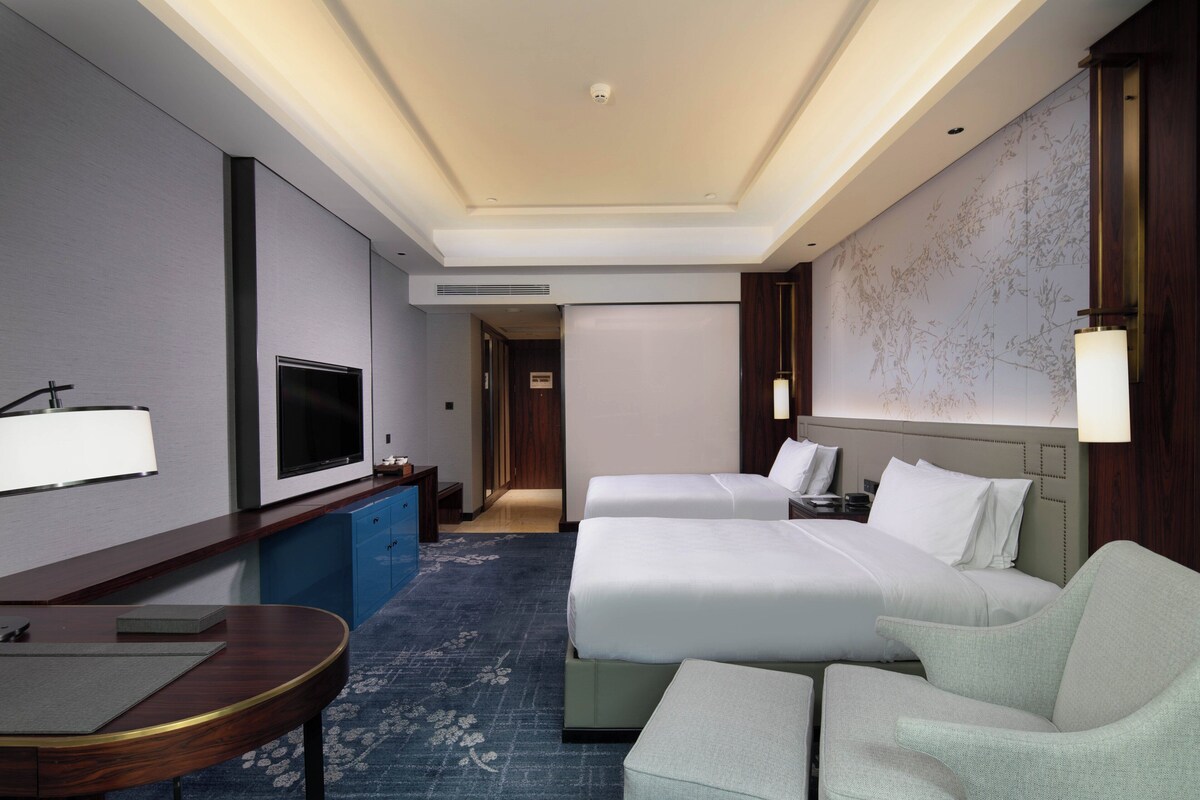 A hotel room with two beds, a desk, a TV, and a map on the wall.