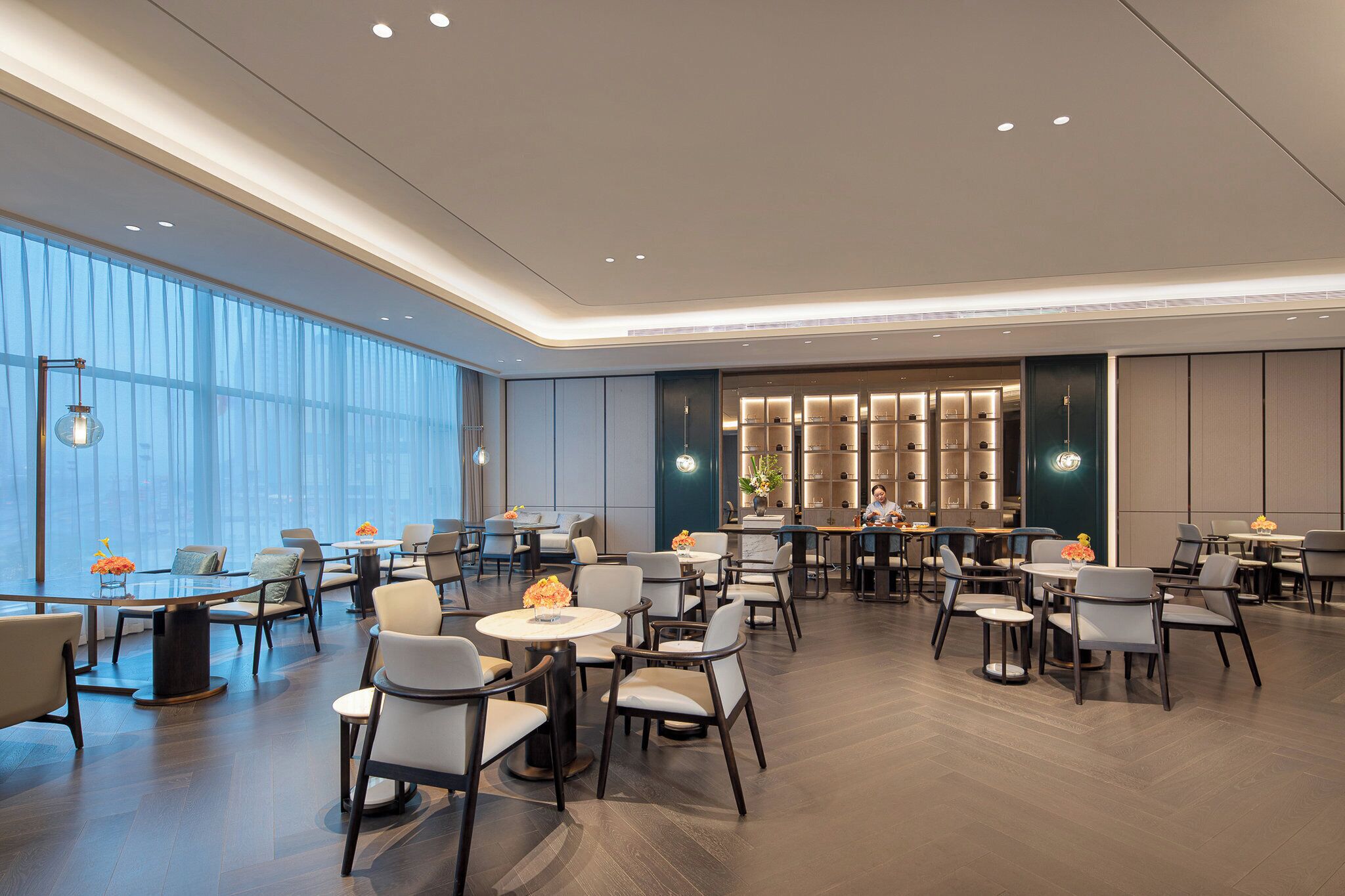 A spacious hotel dining area with multiple tables and chairs, large windows, and a modern interior design.