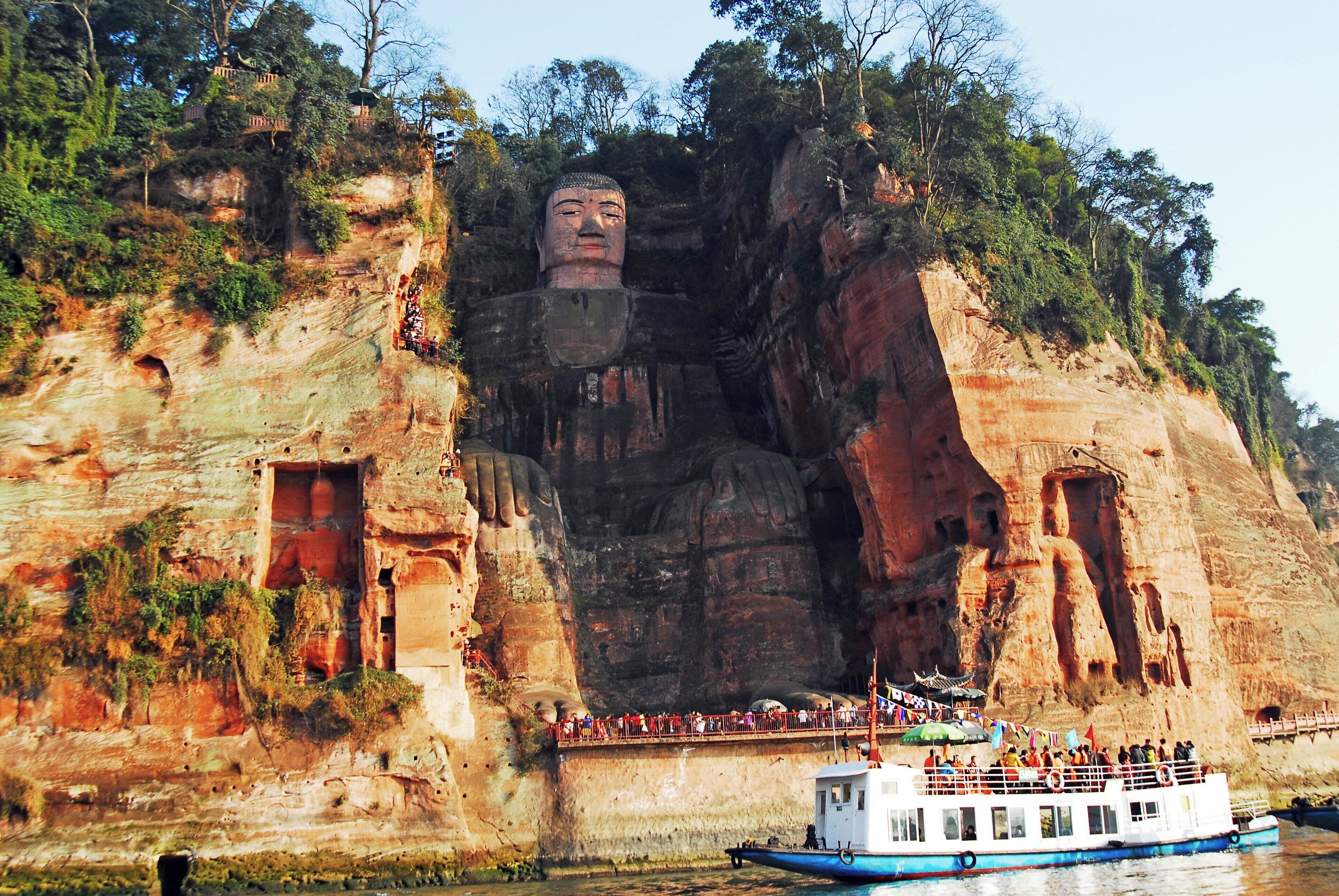 A large Buddha statue carved into a cliffside, with a boat docked in front.