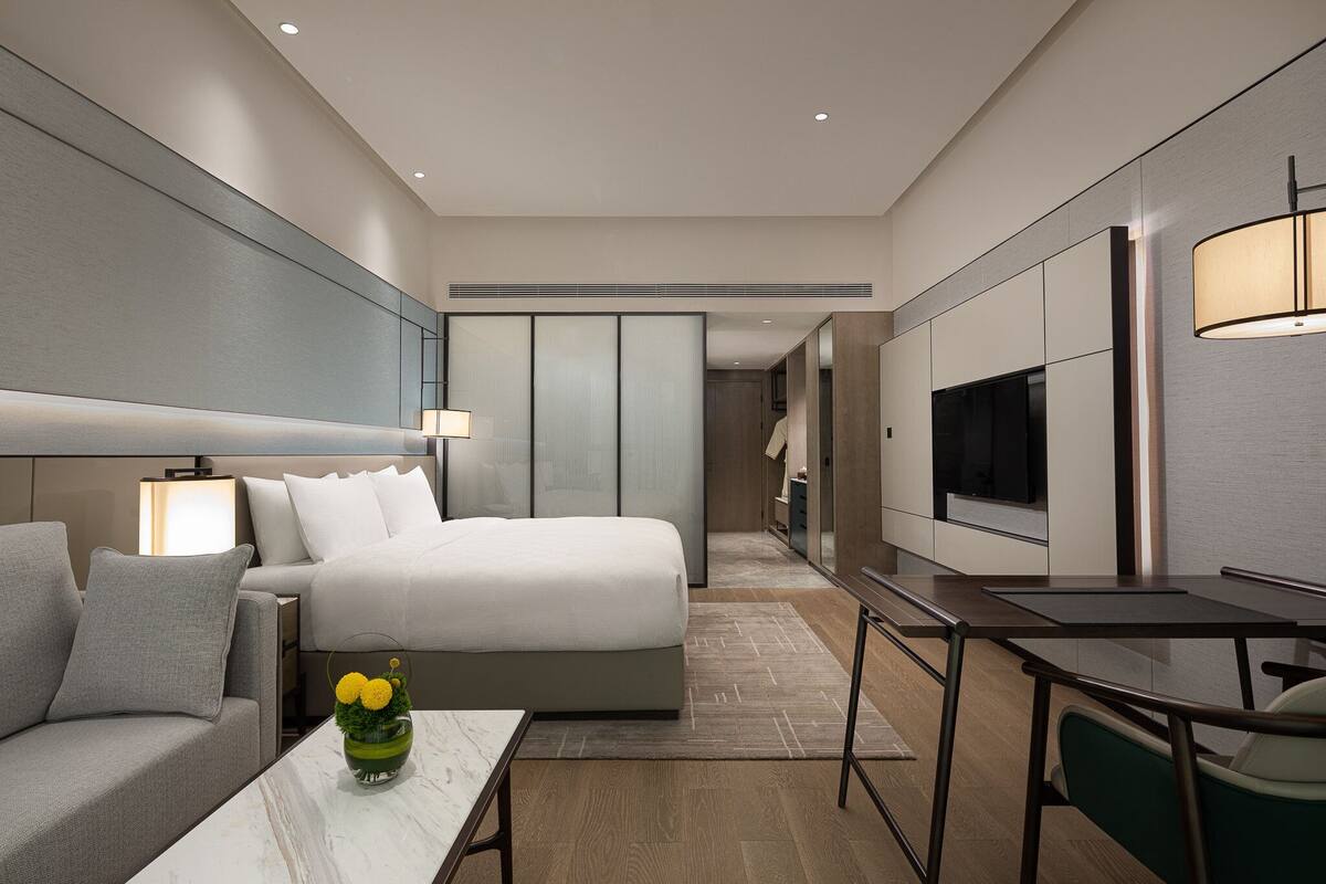 A modern hotel room with a bed, a desk, a TV, and a bathroom visible through a sliding door.