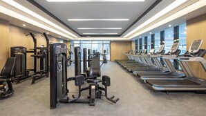 A gym with various exercise machines, treadmills, and a large window providing a view of the city. - HUALUXE Leshan by IHG (Leshan)