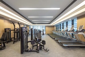 A gym with various exercise machines, treadmills, and a large window providing a view of the city. - HUALUXE Leshan by IHG (Leshan)