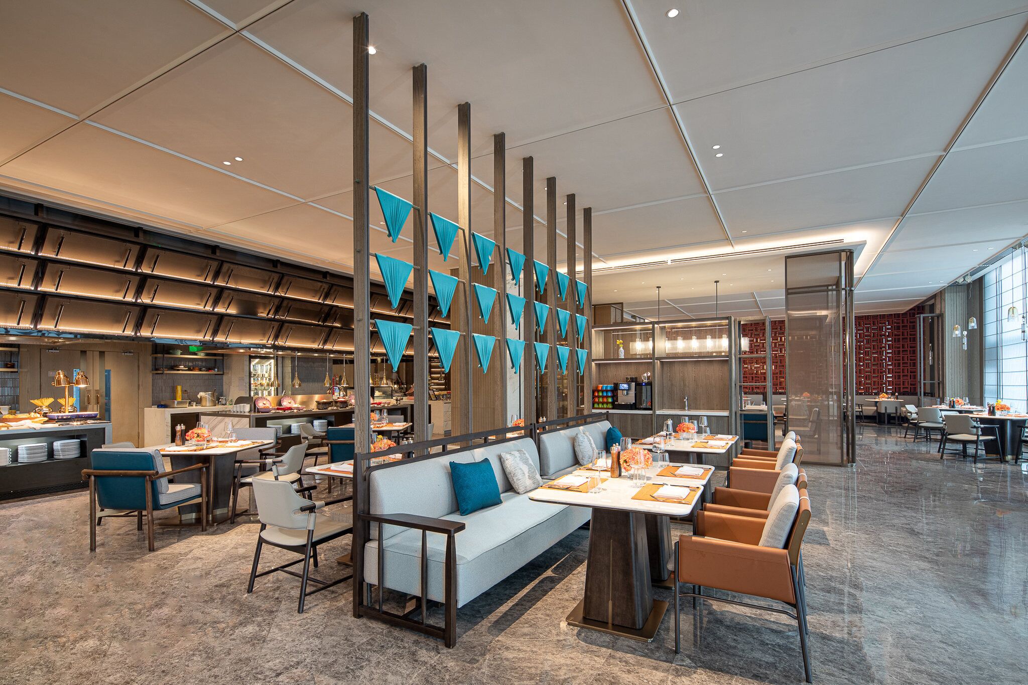 A modern restaurant with a long counter, seating area, and a kitchen in the background.