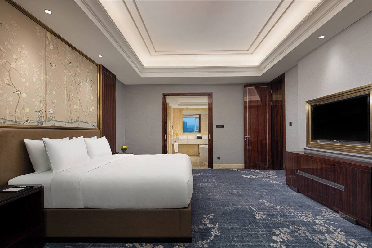 A hotel room with a large bed, a flat-screen TV, a wooden headboard, and a large wall mural.