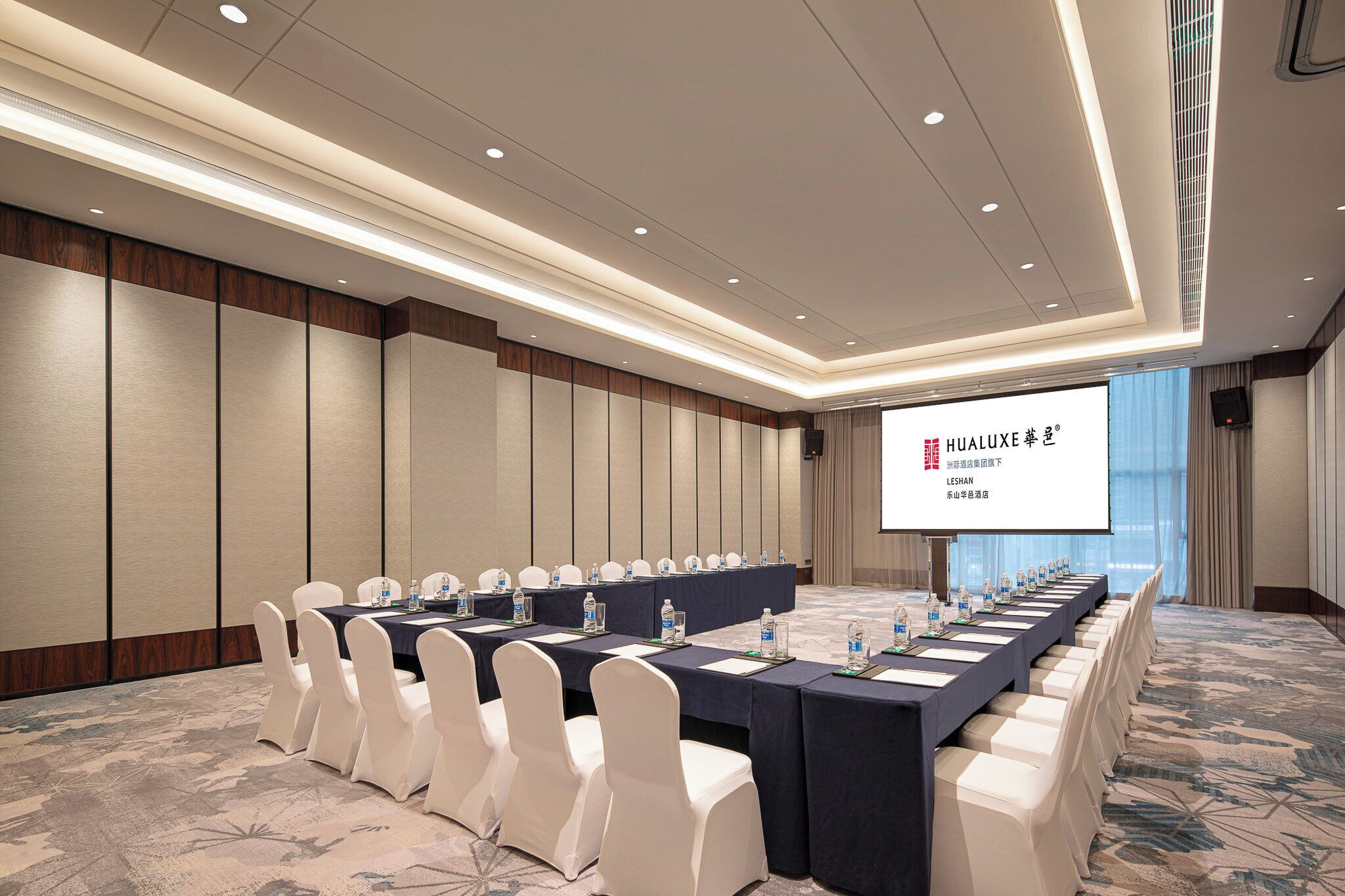 A conference room with a long table, white chairs, and a projection screen displaying text.