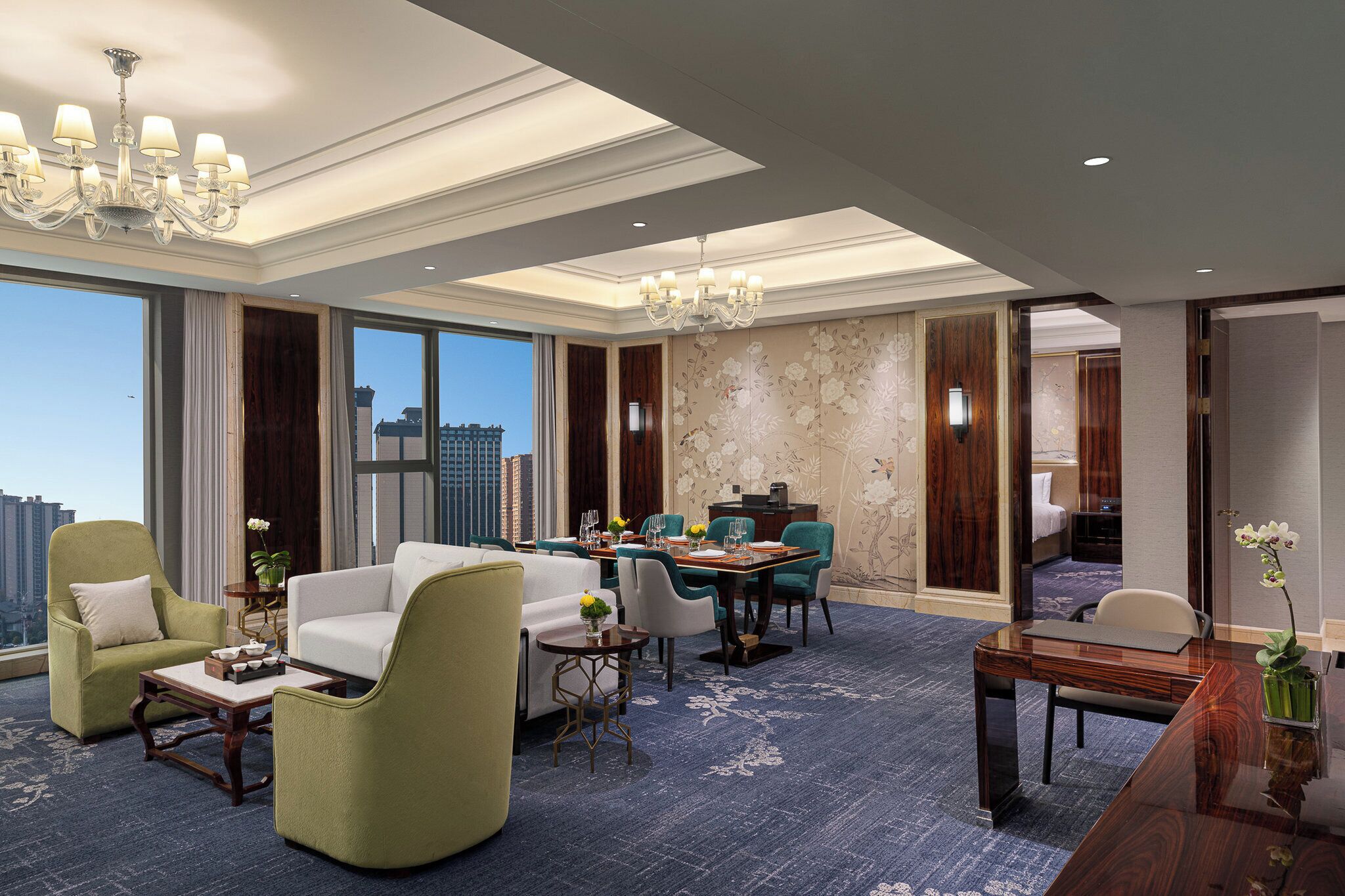 A spacious hotel room with a large seating area, a dining table, and a view of the cityscape.