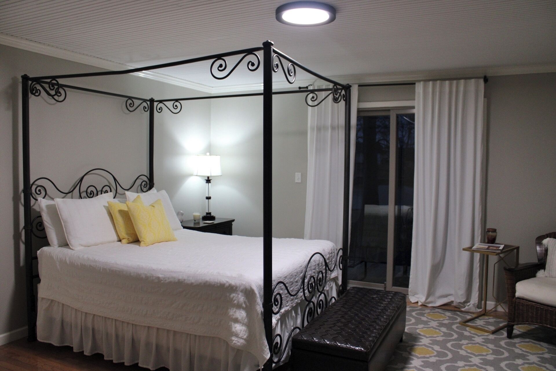 A four-poster bed with a nightstand, a lamp, and a chair in a hotel room.
