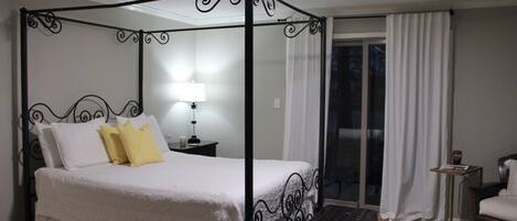 A four-poster bed with a nightstand, a lamp, and a chair in a hotel room.