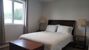Una cama bien tendida con un cabecero de madera, dos lámparas de noche y una mesita de noche de madera con una lámpara.