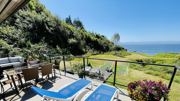 A balcony with lounge chairs, a table, and chairs, overlooking a scenic view of the sea and greenery. - Points West Oceanfront Resort 1 Bed Ocean Point Suite B (Sooke)