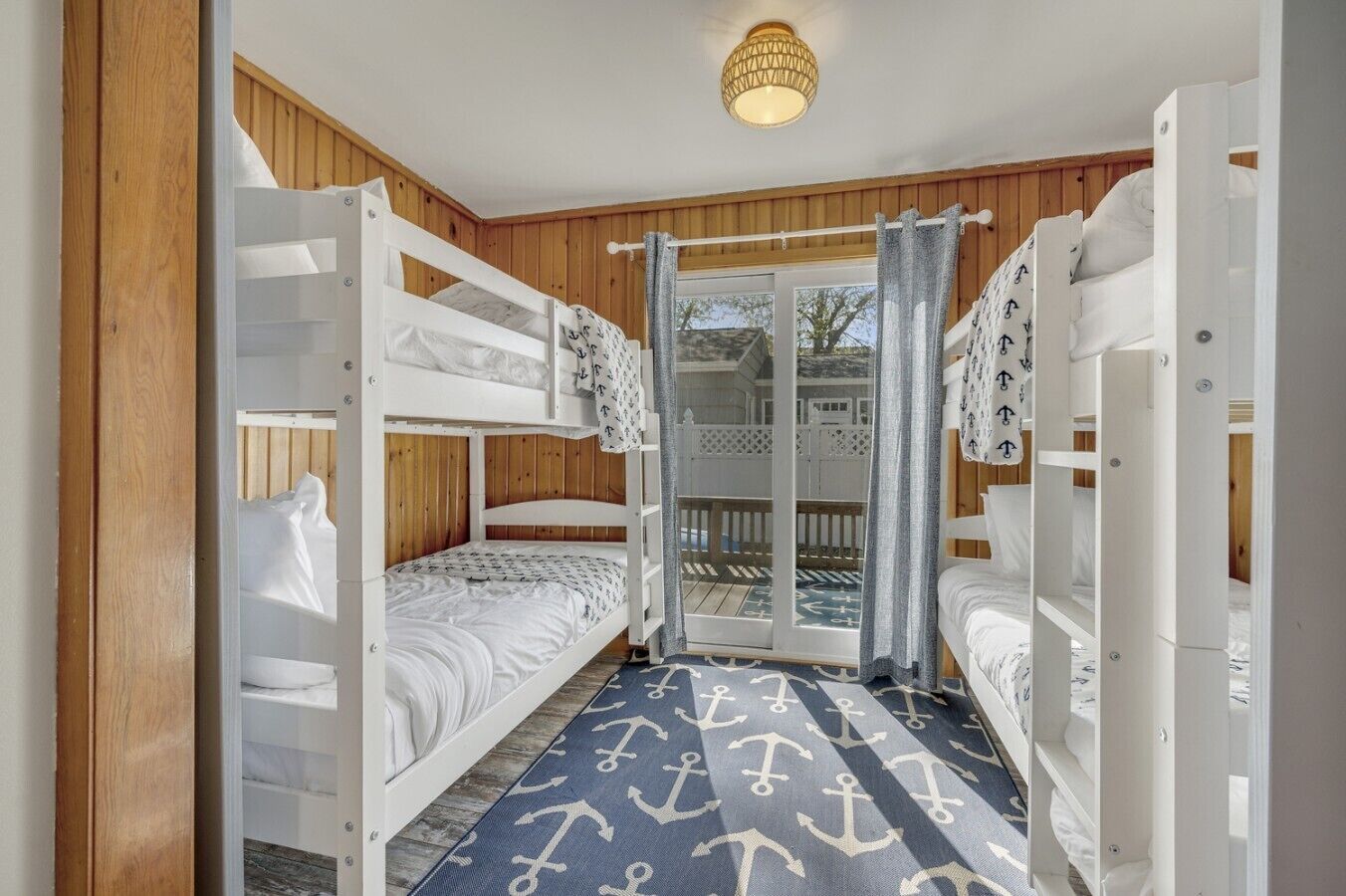 Une chambre avec des lits superposés, un plancher en bois, un tapis à motifs et une vue sur l’extérieur grâce à une porte vitrée.