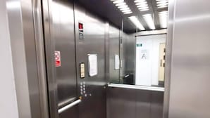 Interior de un ascensor con paredes metálicas, un panel de control y una puerta con un cartel.