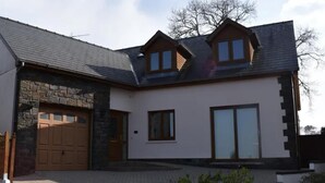 Una casa moderna de dos pisos con fachada de piedra, un garaje y un amplio ventanal corredizo.