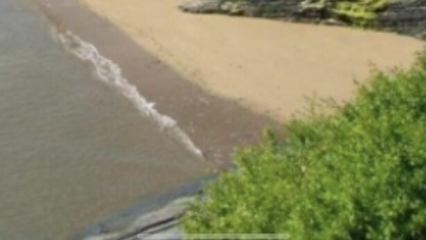 Una playa con algunas personas, un litoral rocoso y edificios al fondo.
