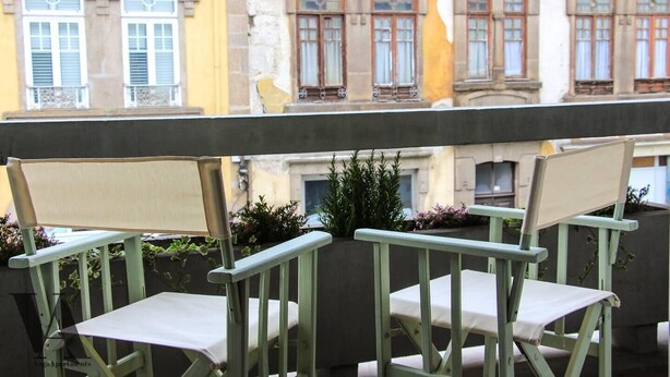 A balcony with two chairs and a table, overlooking a row of buildings with multiple windows. - Beautiful 3-Bed Apartment in Porto, Portugal (Porto)