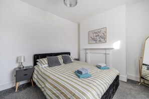 Un dormitorio con cama, mesita de noche, lámpara y un cuadro en la pared.