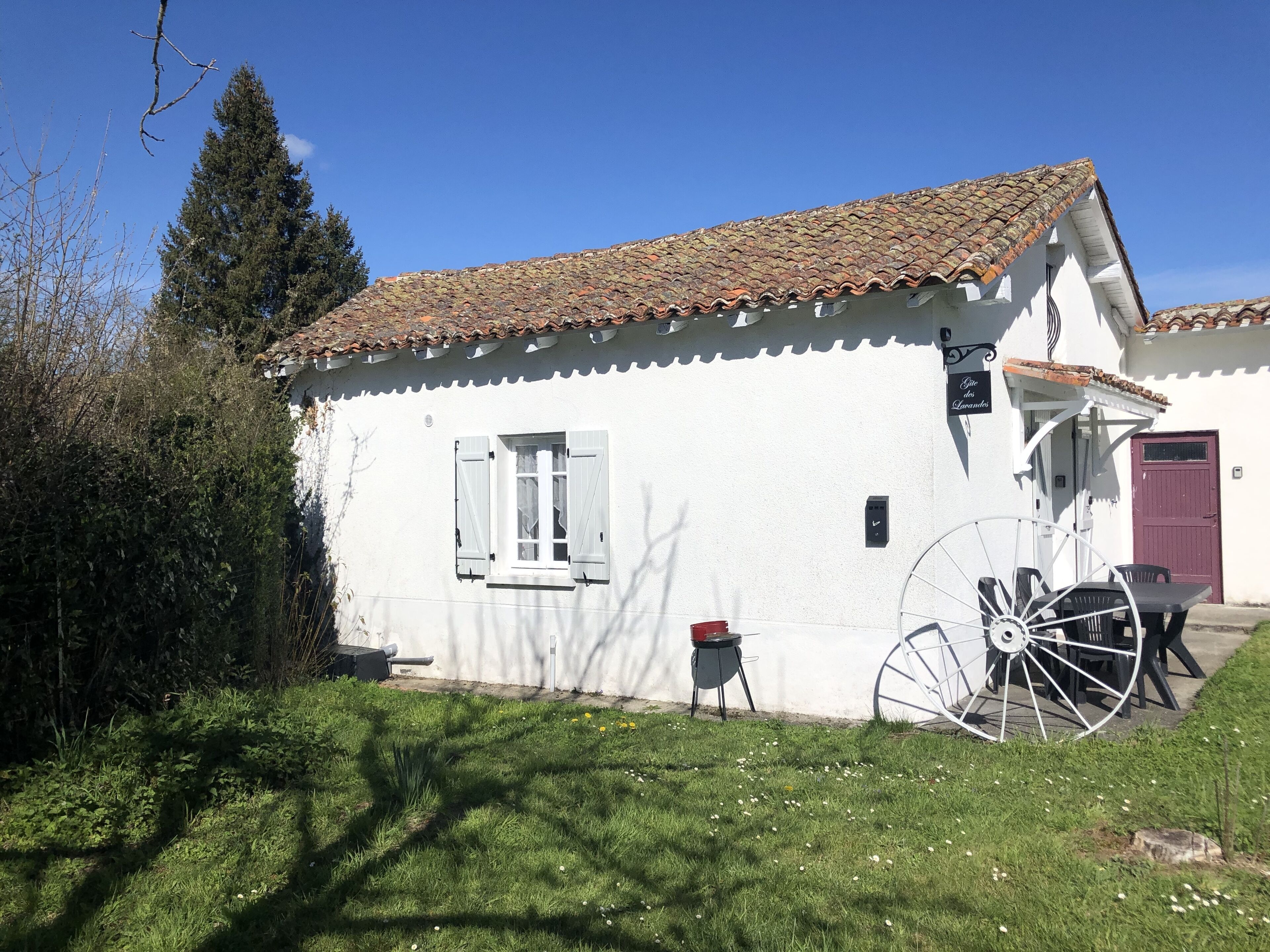 A white building with a tiled roof, a window with shutters, and a large wheelbarrow.