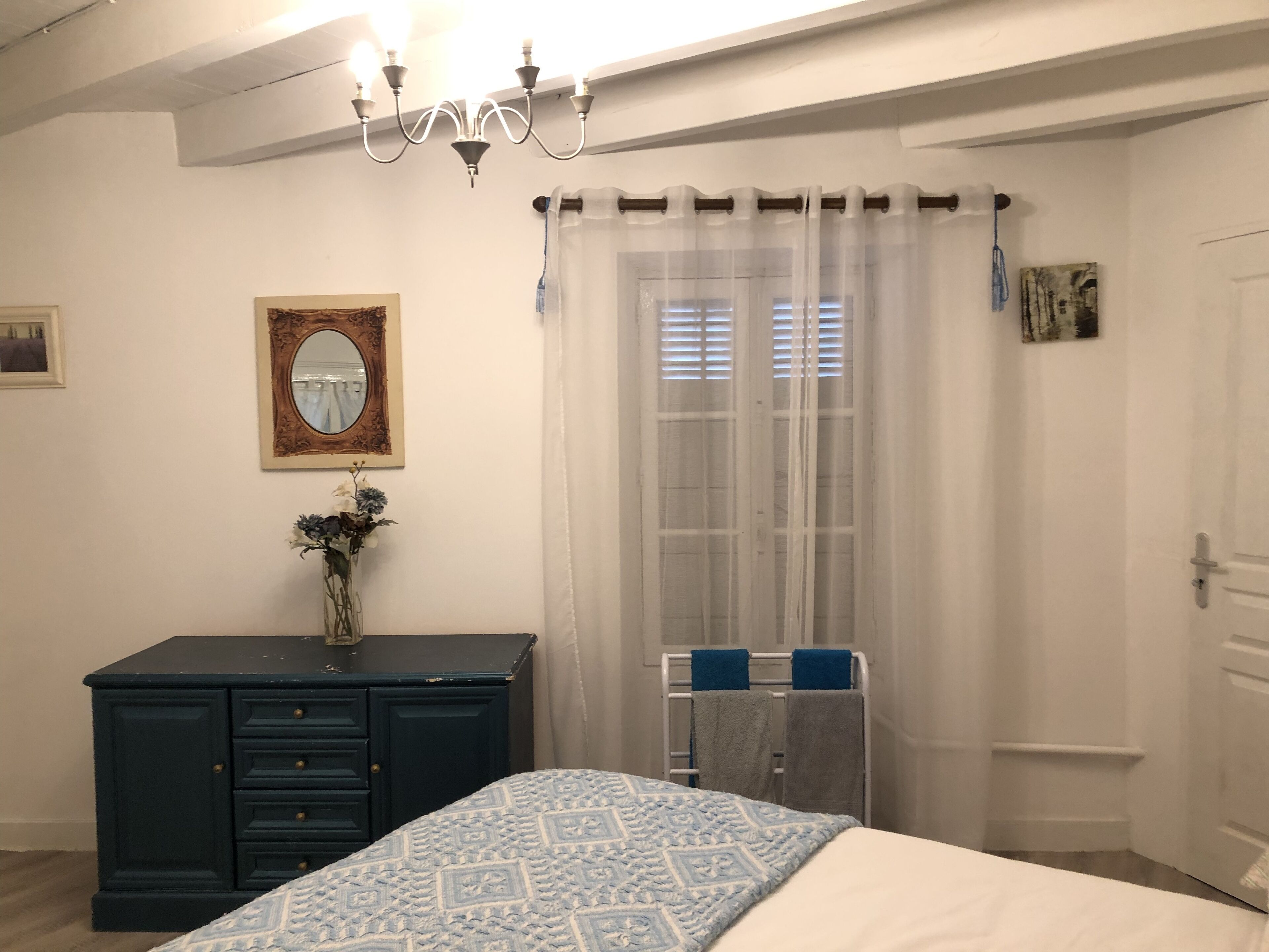 A bedroom with a bed, dresser, mirror, and a window with curtains.