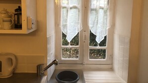 Pieni kylpyhuone, jossa on ikkuna, pesuallas ja hylly, jossa on keittiötarvikkeita.