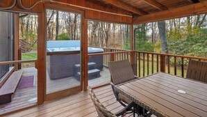 Une terrasse couverte avec un jacuzzi, des sièges d’extérieur et une vue sur la forêt environnante.