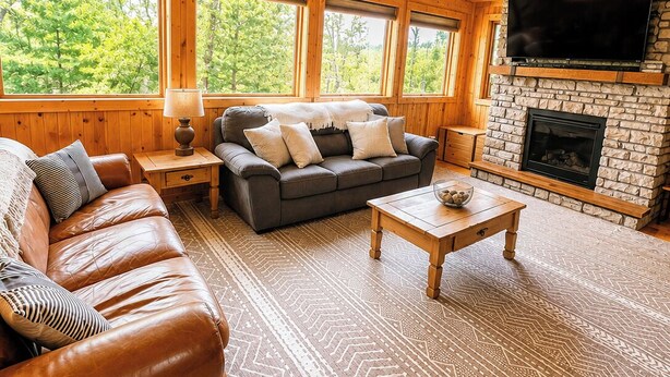 L'intérieur d'une cabane en rondins, avec une cheminée, un canapé en cuir et un téléviseur.
