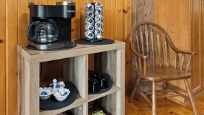 Un petit meuble en bois servant de coin café, avec une machine à café, une pile de tasses et une chaise.
