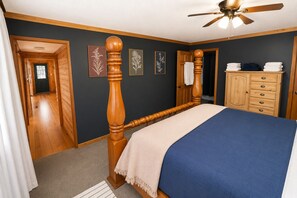 Une chambre à coucher avec un lit en bois, un ventilateur de plafond, une commode et des œuvres d’art encadrées accrochées au mur.