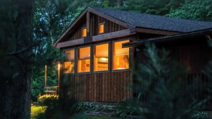 Une cabane en bois dotée de grandes fenêtres, entourée d’arbres.
